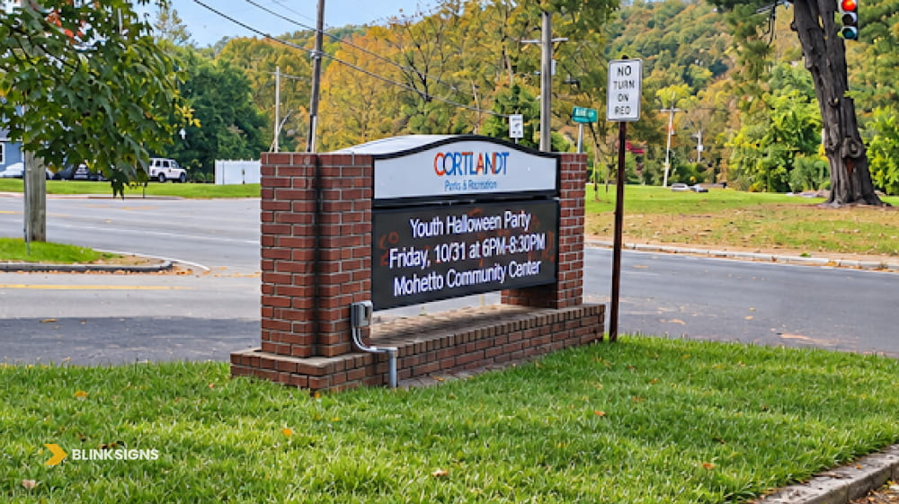 Roadside brick monument sign with digital LED electronic message board displaying community event announcements.