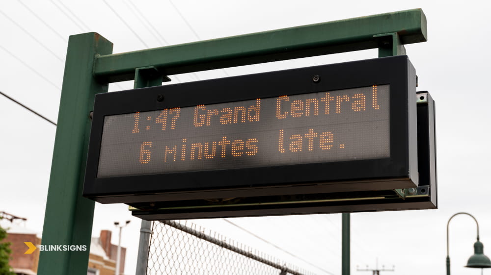 Overhead outdoor digital LED transit display board showing real time train arrival information and delays.